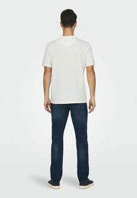 Maglietta bianca in cotone con scollatura rotonda, maniche corte e vestibilità comoda, abbinata a jeans blu scuro e sneakers casual.