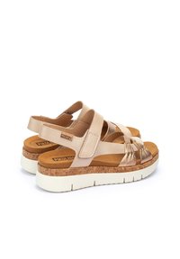 Sandali beige con suola in sughero e suola esterna in gomma bianca. Presentano cinturini incrociati e un accento metallico testurizzato sulla punta.
