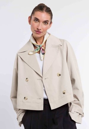 Beige cropped jacket with double-breasted design, large gold buttons, and turn-down collar. Textured fabric and cuff detail with ties.