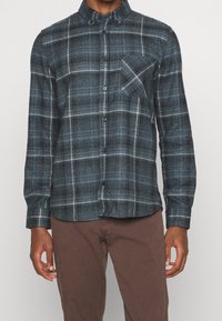 Blauwe geruite overhemd met lange mouwen, gemaakt van textuurstof. Heeft een button-down kraag, voorste knopen en een borstzak.