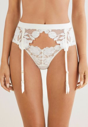 Lingerie in pizzo bianco con motivi floreali, un design aperto e spalline in satin, con una vita liscia e dettagli di reggicalze regolabili.