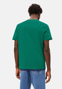 Grünes Baumwoll-T-Shirt mit kurzen Ärmeln und Rundhalsausschnitt. Verfügt über eine glatte Textur und eine gleichmäßige Verarbeitung auf der Rückseite. Kombiniert mit blauen Jeans.