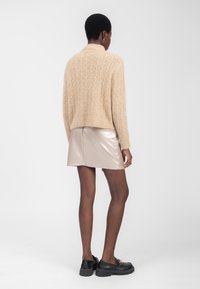Beige fuzzy sweater med høj krave, parret med en kort, skinnende pink nederdel. Modellen har sorte slip-on sko med en tyk sål på.