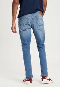 Lichtblauwe slim-fit jeans met een mid-waist, voorzien van vijf zakken en een bruin leren label op de tailleband. gedragen met witte sneakers.