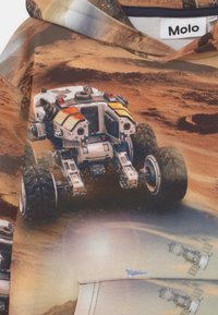 Marsovský rover s velkými koly prochází červenou skalnatou krajinou, s malými satelity a sluncem v pozadí na látce.