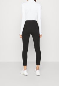 Svarta leggings med hög midja, gjorda av ett mjukt, stretchigt material. Bärs med en åtsittande vit topp och vita sneakers.