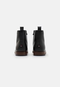 Černé kožené kotníkové boty s hladkým povrchem, hnědou podrážkou, zipovým uzávěrem a malým logem na patě.