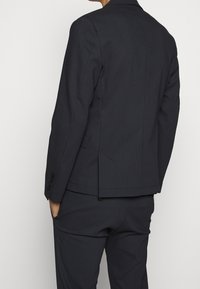Giacca da abito a quadri blu scuro con vestibilità sartoriale, rever a punta e polsini con quattro bottoni. Le aperture laterali offrono libertà di movimento. Design strutturato.