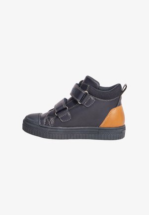 Zwarte hoge schoen met twee klittenbandsluitingen, rubberen zool, ronde neus en een tan leren accent op de hak. Glad textuur met stiksels.