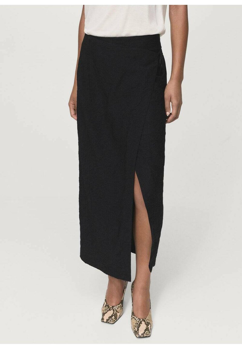 Falda negra ajustada con una abertura lateral, tejido texturizado y un diseño de cintura alta. Combinada con zapatos de tacón altos con estampado.