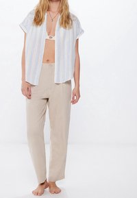 Chemise légère à manches courtes boutonnée, rayée bleu et blanc, associée à un pantalon beige ample avec une fermeture à un seul bouton.