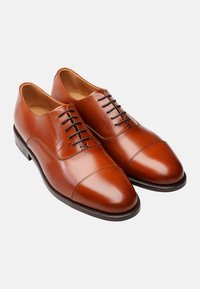 Chaussures habillées en cuir marron, avec une finition lisse, un bout rond et un design à lacets. Présente un bout cap et une semelle sombre contrastante.