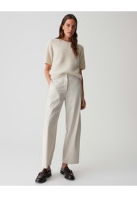 Helles Creme, strukturiertes, kurzärmliges Strickpullover kombiniert mit maßgeschneiderten, hoch sitzenden, hellen Hosen. Dunkle Loafers runden das Outfit ab.