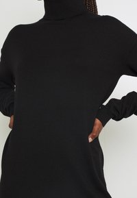Schwarzer Rollkragenpullover mit langen Ärmeln, aus dickem Strickstoff gefertigt, mit lässiger Passform und seitlichen Schlitzen für mehr Bewegungsfreiheit.