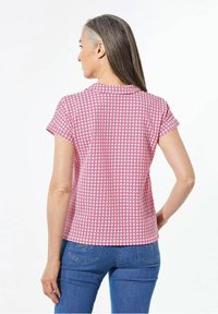 Korte mouw top in een roze en wit geometrisch patroon, met een ronde kraag en zachte stof. Draagt met blauwe spijkerbroek.