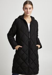 Cappotto lungo trapuntato nero con zip, cappuccio e tasche laterali. Presenta un motivo a diamante per texture. Tessuto morbido con una finitura liscia.