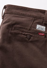 Gros plan d’un pantalon marron Levi’s montrant une poche arrière avec bouton, une passants de ceinture et des étiquettes en tissu à la marque Levi’s.