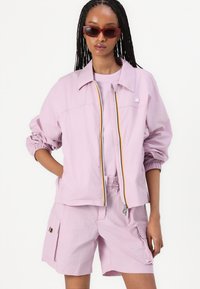 Lichtroze lichte jas met elastische manchetten en een kleurrijke rits. Gecombineerd met bijpassende shorts met zakken en gestreepte details.