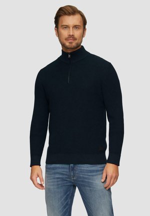 Dunkelblauer Strickpullover mit hohem Kragen und Viertelreißverschluss. Verfügt über gerippte Säume und einen gerippten Saum für einen strukturierten Look. Jeans aus Denim vervollständigen das Outfit.