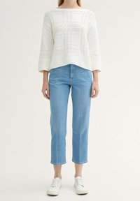 Vit stickad tröja med ett strukturerat, randigt mönster, kombinerad med ljusblå cropped jeans och vita sneakers.