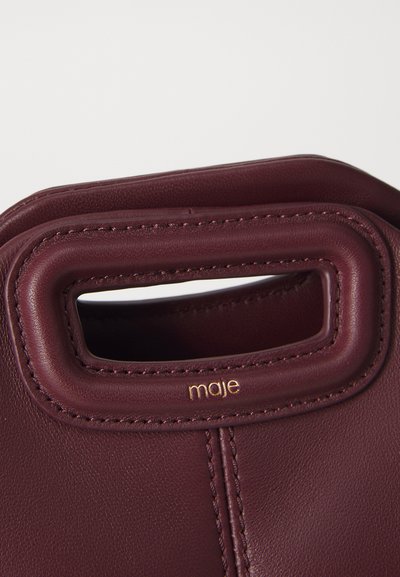 Burgundy nahkalaukku, jossa on pyöreä, leikattu kahva ja näkyvät saumat. Brändin nimi "maje" on kullattuna painettuna kahvassa.