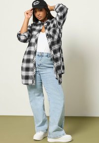 Svart och vit rutigt stor oversized skjorta med långa ärmar, kombinerad med ljusblå högmidjade jeans och vita sneakers. Svart keps som accent.