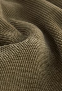 Prążkowana brązowa tkanina, teksturowana delikatnymi pionowymi liniami, miękka i elastyczna, ukazująca ciepły, neutralny kolor odpowiedni do różnych zastosowań.