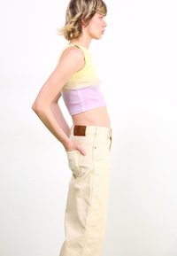 Top court rayé en jaune et lavande, associé à un jean taille haute beige avec une patch en cuir à l'arrière et des poches latérales.