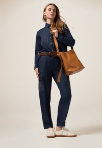 Completo in denim con maniche lunghe, caratterizzato da una chiusura frontale con bottoni e decorazioni luccicanti. Abbinato a una cintura marrone e una borsa in pelle beige.