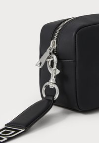 Black rectangular bag made of faux leather, featuring a silver zipper and hardware. Includes a flat, detachable strap with a patterned accent.