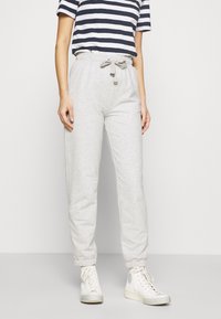 Světle šedé tepláky s elastickými manžetami a páskem se stahováním, v kombinaci s námořnicko-modrým a bílým pruhovaným tričkem a bílými teniskami.