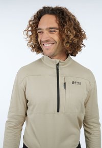 Beżowy pulower z mikrofleecu z kołnierzem na stójce, półzamkiem z przodu, kieszenią na piersi oraz czarnym zamkiem; na lewej piersi znajduje się logo.