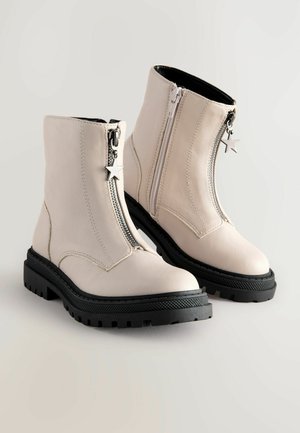 Botine albe din piele, cu fermoare laterale și taburi în formă de stea, având o talpă din cauciuc negru texturat și un model de tread robust.