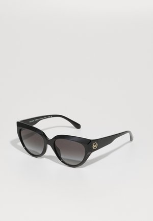 Sunglasses with a black plastic frame, angular design, gradient dark lenses, and a gold logo accent on the side.