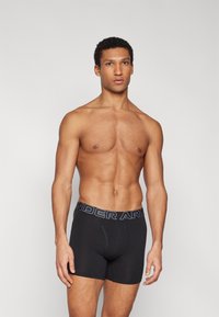 Fekete boxer alsónadrág puha anyagból, márkázott rugalmas derékpánttal, melyen "UNDER ARMOUR" felirat található szürkében, klasszikus designnal és testhezálló szabással.