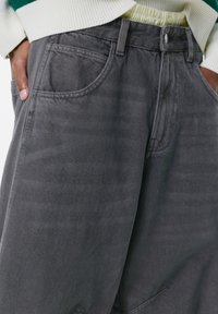Graue Denim-Hosen haben einen lockeren Schnitt, fünf Taschen, einen Knopfverschluss und eine dezente Textur, die das Gewebe betont.