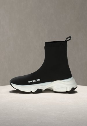 Mustad kõrge säärega sokksneaker paksu valge tallaga ja "LOVE MOSCHINO" tekstiga küljel, eksponeeritud helehalli pinna ja tausta peal.