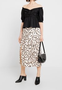 Top bez ramínek v černé barvě s peplum stylem, v kombinaci s bílou sukní s hnědým skvrnitým vzorem, doplněn é černými podpatkovými muly a malou kabelkou.