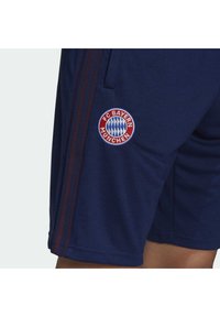 Pantaloni corti da atletica blu navy con tre strisce laterali rosso scuro, caratterizzati da un logo ricamato del FC Bayern München sulla coscia sinistra.