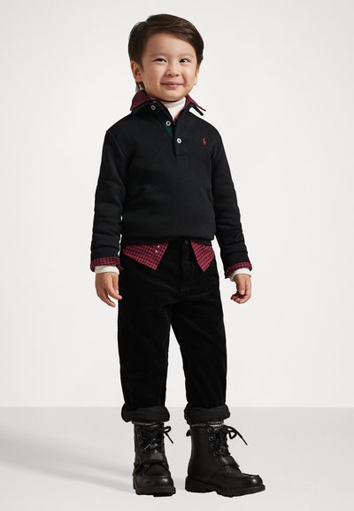 Μαύρη μπλούζα με πράσινο και λευκό γιακά, κόκκινο καρώ πουκάμισο από κάτω, μαύρο βελούδινο παντελόνι, μαύρες δερμάτινες μπο boots με γκρι επένδυση.