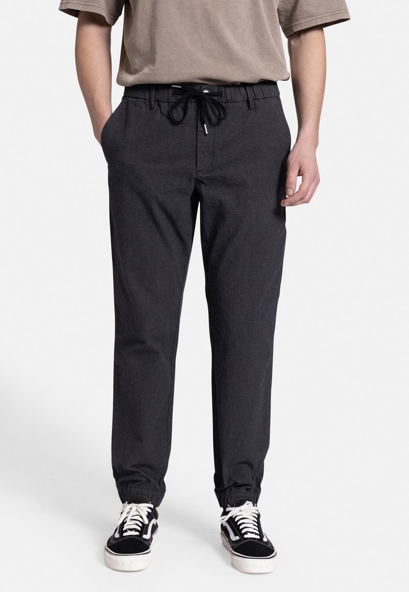 Mørkegrå joggebukser med elastisk talje, justerbar snor, sidelommer og elastiske manchetter. Båret med sorte sneakers.