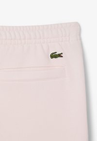 Lichtroze sportshorts met een elastische tailleband en een klein groen krokodillenlogo. Bevat een achterzak en heeft een gladde textuur.