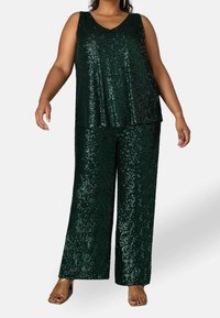 Grön paljettopp med V-hals och lös passform, kombinerad med vida paljettbyxor. Båda plagg har glänsande, reflexiva texturer.