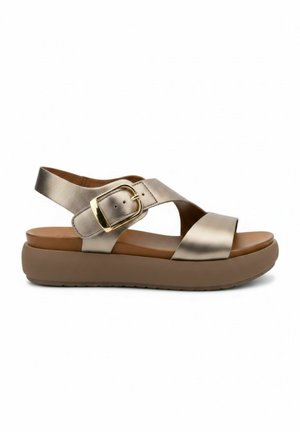 Open teen sandaal met een beige gewatteerde plateauzool, metalen kruisbandjes en een grote gouden gesp op het enkelbandje.