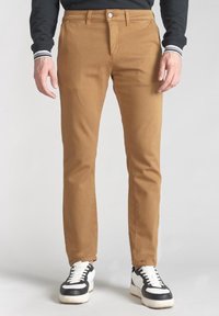 Bruna bomullsbyxor med smal passform, med dragkedja och knappstängning. Tillsammans med svarta och vita sneakers.