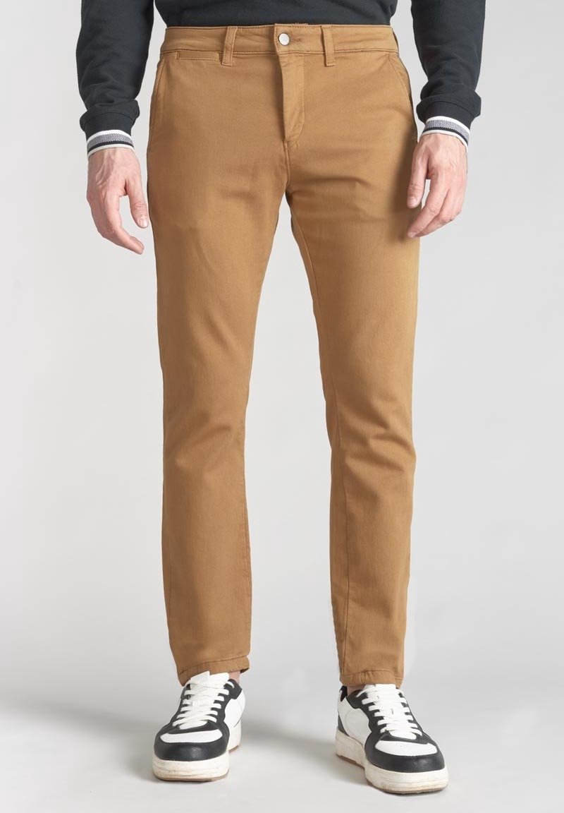 Bruna bomullsbyxor med smal passform, med dragkedja och knappstängning. Tillsammans med svarta och vita sneakers.