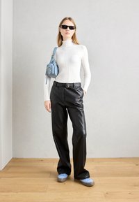 Un col roulé blanc ajusté, un pantalon en faux cuir noir, des baskets bleu clair et un petit sac bandoulière bleu. Design élégant et moderne aux textures douces.
