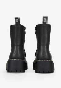 Stivaletti in pelle nera con suola chunky, zip laterali e un inserto con logo. Il dettaglio delle cuciture contrasta con il materiale liscio.