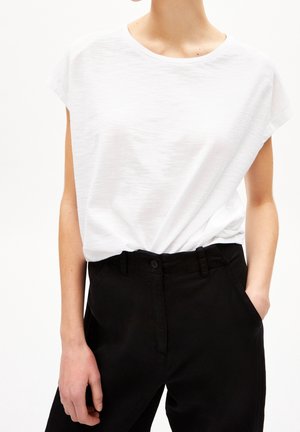 T-shirt blanc à manches courtes en tissu doux, associé à un pantalon noir taille haute avec fermeture à boutons et poches latérales.