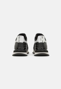 Schwarze Sportschuhe mit einem glänzenden silbernen Absatz, strukturierten Akzenten und einem gemusterten Obermaterial. Verfügt über eine dicke schwarze Sohle mit weißen Streifen.